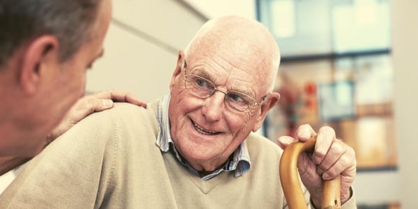 An elderly parent, a gentleman, with dementia that is smiling and talking with his in-home carer in the familiar and comfortable surroundings of his own home.